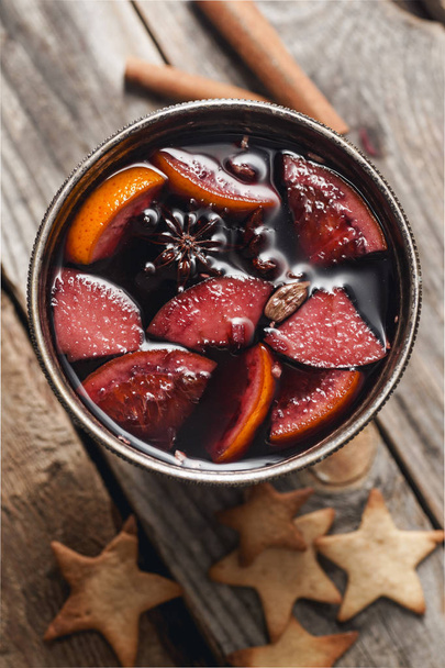Mulled wine with apple and orange slices and cinnamon sticks with gingerbread cookies on wooden background, close-up  - Foto, Imagem