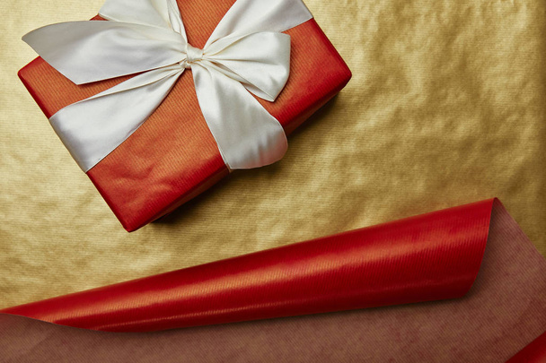 top view of wrapped christmas present with ribbon on red and golden wrapping papers background - Fotoğraf, Görsel