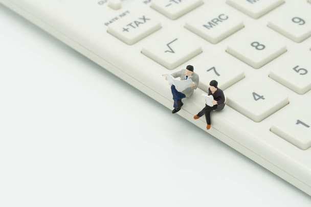 Miniatuur 2 mensen zitten op witte rekenmachine met behulp van als achtergrond bedrijfsconcept en teamwork concept met kopie ruimte en witruimte. - Foto, afbeelding