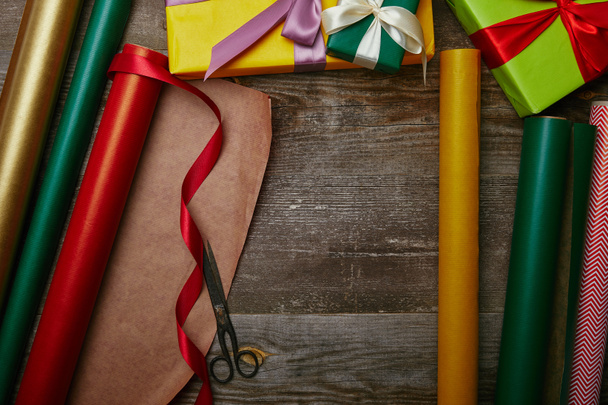 top view of arrangement of wrapping papers, christmas presents with ribbons and scissors on wooden tabletop - 写真・画像