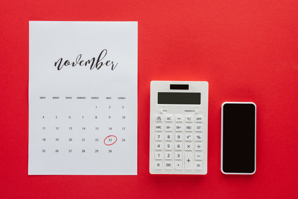 top view of calendar for November, calculator and smartphone isolated on red, black friday concept - Photo, Image