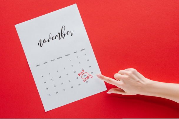 cropped view of woman pointing at black friday in calendar for November isolated on red - Photo, Image