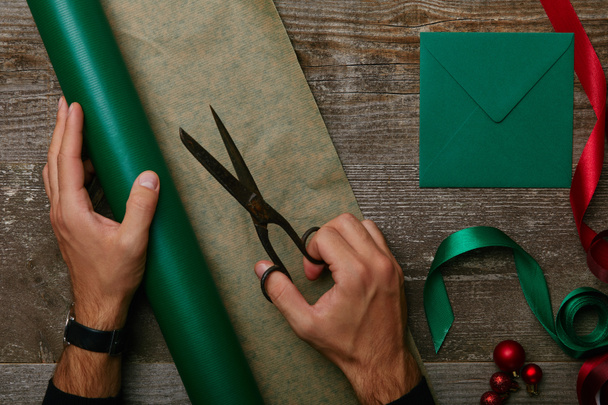 částečný pohled člověka s nůžkami, balicí papír, dárkové balení a obálky na dřevěnou desku - Fotografie, Obrázek