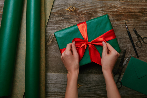 cropped shot of woman tying ribbon on present on wooden tabletop with wrapping paper - 写真・画像