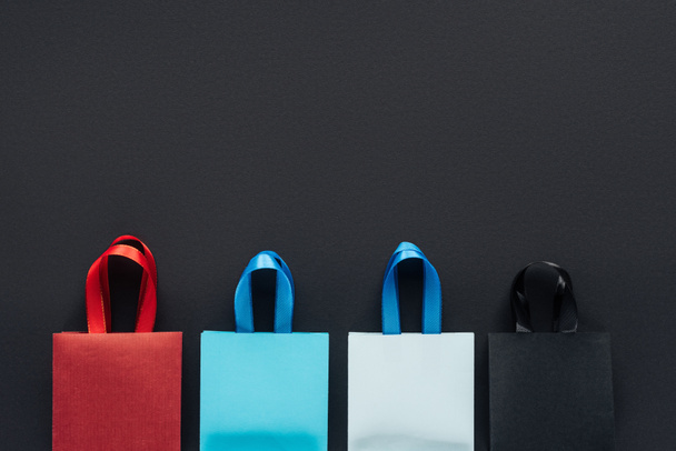 top view of colorful shopping bags on black background with copy space for black friday  - Foto, Imagem
