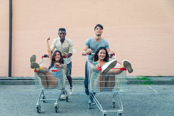 Multi-ethnic group of friends playing with shopping carts in a parking - Fotoğraf, Görsel