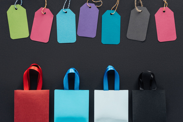 felülnézet színes bevásárló táskák és eladó címkék, fekete háttér, fekete péntek   - Fotó, kép