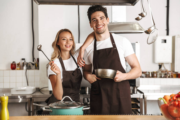 Happy chef couple dressed in aprons cooking together at the kitchen - Foto, immagini