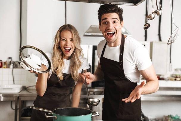 Image of displeased shocked emotional young friends loving couple chefs on the kitchen cooking. - Photo, Image