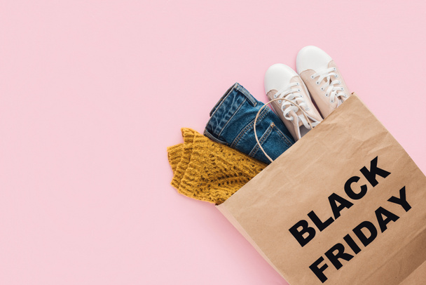 top view of trendy clothes in shopping bag with black friday sign isolated on pink - Photo, Image