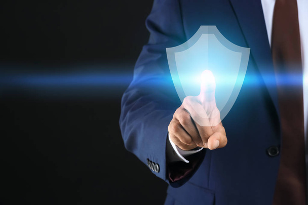 Businessman pressing shield icon on dark background. Data security concept - Photo, Image