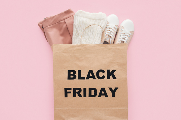 top view of stylish clothes in shopping bag with black friday sign isolated on pink  - Photo, Image