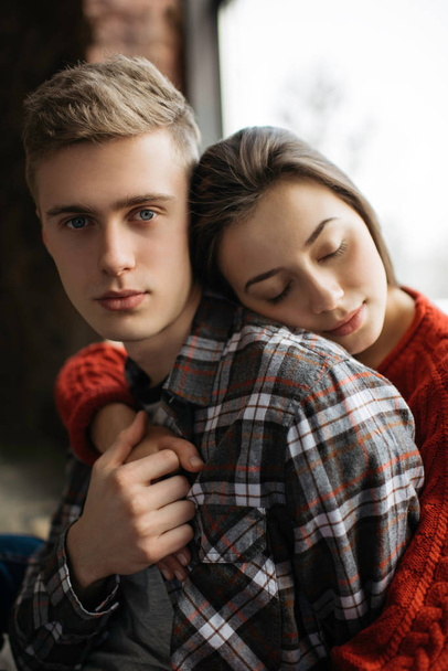 Beautiful lovely couple hugging in cozy loft house. Portrait of young family posing  for camera. Harmony. Relationship. Balance. Boyfriend and girlfriend sitting near window.  - Фото, изображение