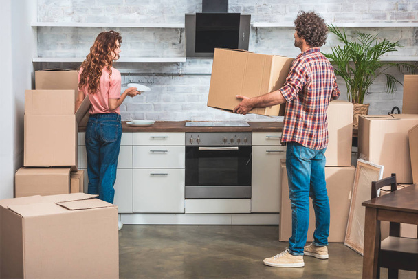 парень и девушка распаковывают посуду из картонных коробок на новой кухне
 - Фото, изображение