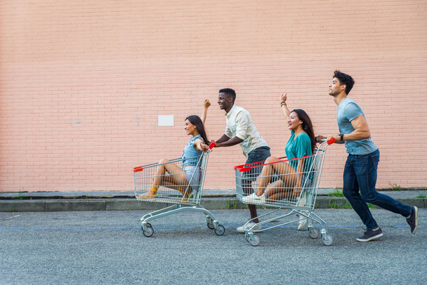 Grupo multiétnico de amigos jugando con carritos de compras en un estacionamiento
 - Foto, Imagen