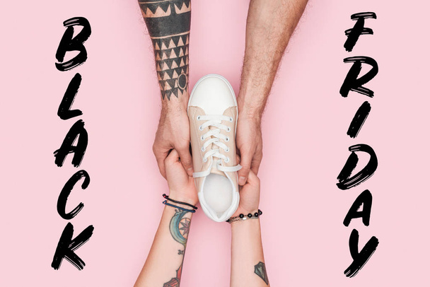 vista recortada de los adictos a las compras tatuados sosteniendo zapatilla aislada en rosa con letras de viernes negro
  - Foto, Imagen
