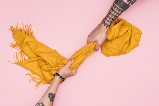 vista parcial de clientes tatuados tirando de bufanda amarilla aislada en rosa
 - Foto, imagen