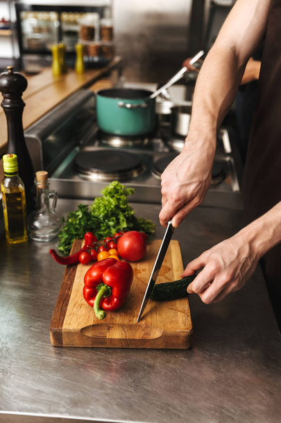 Close up van de handen van een man hakken van groenten op een snijplank op hij keuken - Foto, afbeelding