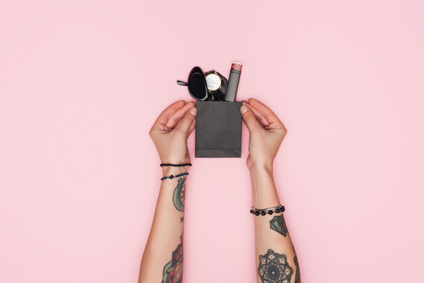 gedeeltelijke weergave van getatoeëerd meisje houden weinig boodschappentas met stijlvolle accessoires geïsoleerd op roze - Foto, afbeelding