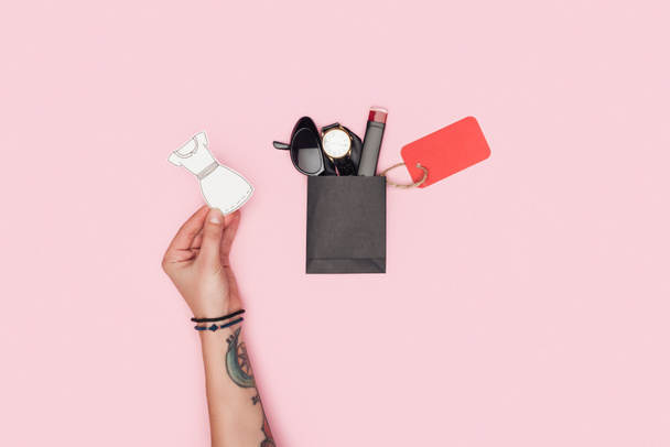 vista recortada de niña sosteniendo vestido de papel cerca de pequeña bolsa de compras con accesorios y etiqueta de venta para el viernes negro aislado en rosa
 - Foto, Imagen