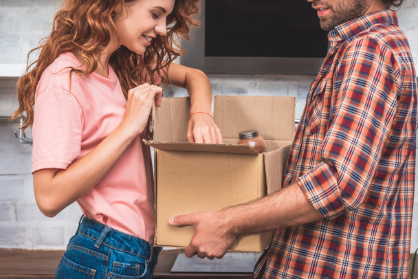 cropped image of couple unpacking cardboard box at new home - Photo, Image