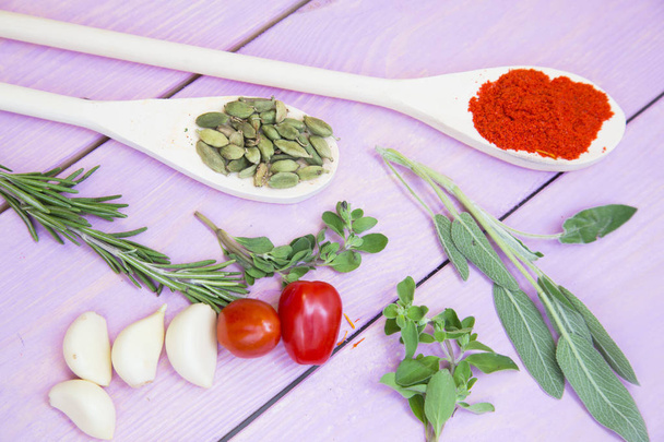 Cooking Hot Spicy Food Concept. Dry spices,beans and herbs in wooden spoons,fresh tomatoes and herbs, purple wooden background, top view - Fotó, kép