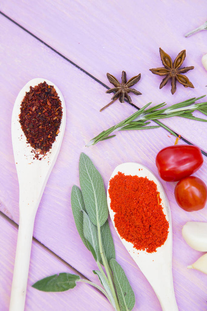 Cooking Hot Spicy Food Concept. Dry spices,beans and herbs in wooden spoons,fresh tomatoes and herbs, purple wooden background, top view - Fotografie, Obrázek