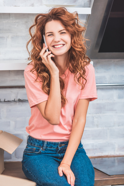 счастливая молодая женщина разговаривает по смартфону и улыбается на камеру во время переезда домой
 - Фото, изображение