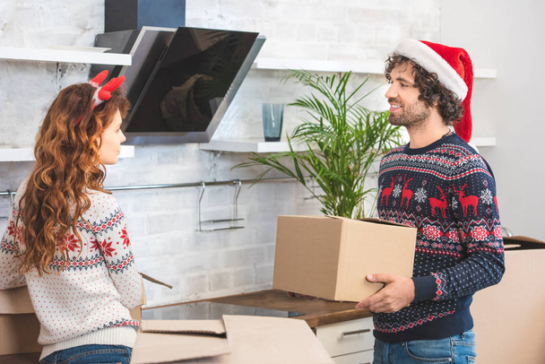 happy young couple unpacking cardboard boxes in new home at christmastime  - Photo, Image