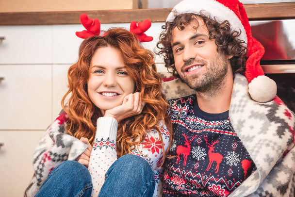 glückliches junges Paar mit Weihnachtsmann-Hut und Geweih-Stirnband lächelt gemeinsam in die Kamera - Foto, Bild
