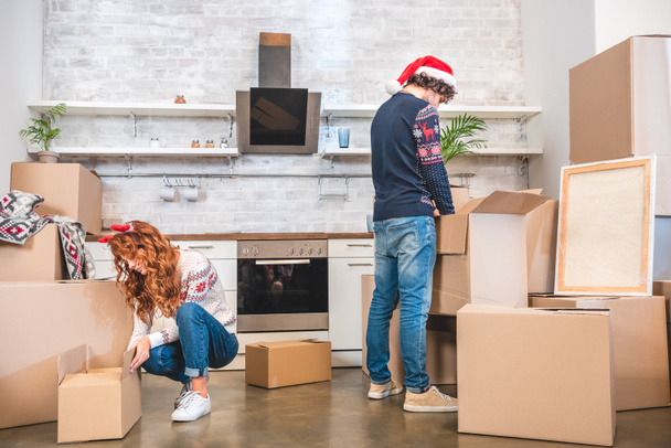 young couple unpacking cardboard boxes in new apartment at christmastime - Photo, Image