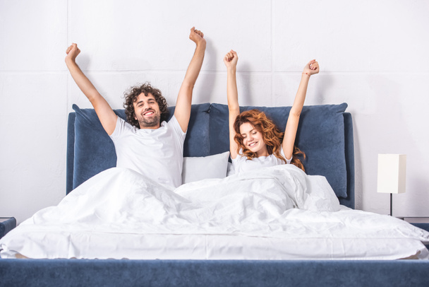 glückliches junges Paar breitet Arme aus und wacht gemeinsam im Schlafzimmer auf  - Foto, Bild