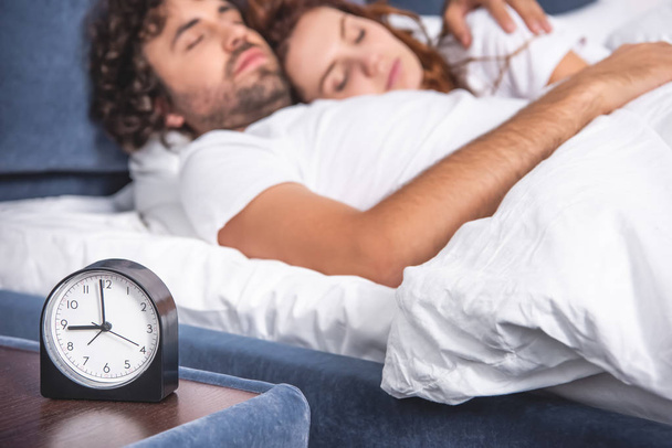 close-up view of alarm clock and young couple sleeping together behind - Photo, image