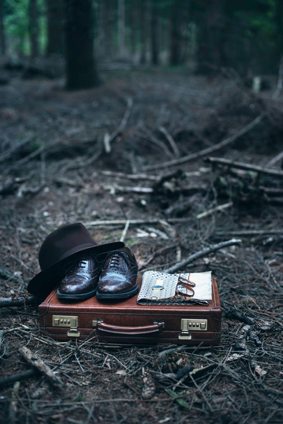 Εγκαταλελειμμένο χαρτοφύλακα με παπούτσια, καπέλο, γυαλιά, το ρολόι και σάλι στο δάσος. - Φωτογραφία, εικόνα