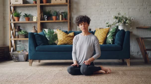 Female yoga teacher is demonstrating King Pigeon pose, talking to social media subscribers and smiling looking at camera. Vlogging and sports concept. - Felvétel, videó