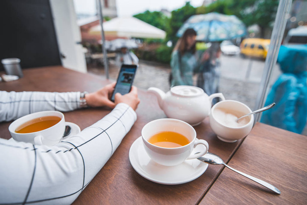 Paar sitzt im Café und trinkt warmen Tee an einem kalten Herbsttag. Frau fotografiert am Telefon für Instagram. Ego-Ansicht - Foto, Bild