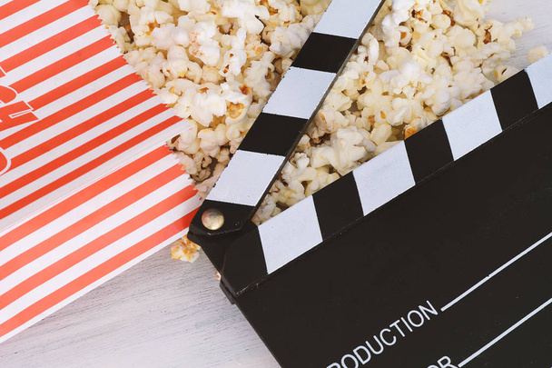 Tasty popcorn and clapboard on white wooden background. Cinema concept - Fotoğraf, Görsel