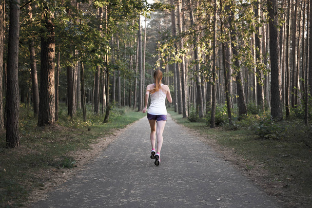 Jeune fille maigre rousse blanche courant dans la forêt. Bonjour, jogging. Vue de dos
. - Photo, image
