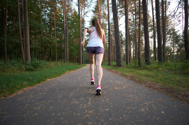 Young white redhead skinny girl running in the summer forest. Jogging at morning. View from back. - Photo, Image