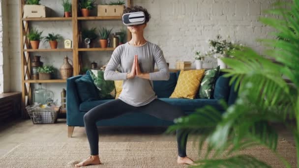 Cute girl is doing stretching exercises at home wearing artificial reality glasses enjoying amazing experience using modern device. Sports and technology concept. - Záběry, video