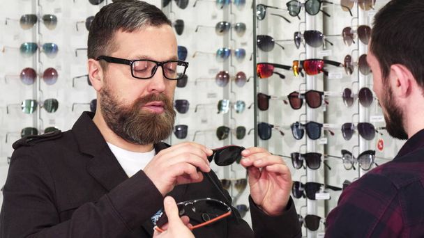 Optometrista profesional mostrando gafas para la venta a su cliente masculino
 - Foto, imagen