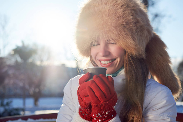 Rossa ragazza magra, indossato in cappello di pelliccia di volpe e giacca bianca, bere caffè per andare in inverno giorno freddo e ridere
.  - Foto, immagini