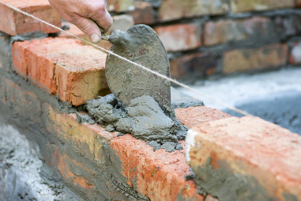 Bricklayer usando espátula para bater um nível de tijolo. Mão cimento branco-lavagem construído parede tijolo nova casa, trabalhador pedreiro instalação de alvenaria tijolo na parede exterior com espátula faca de vidraceiro
 - Foto, Imagem