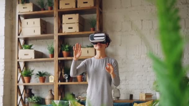 Amazed young lady is enjoying new experience in augmented reality glasses standing in flat and moving hands reaching in syberspace. Technology and fun concept. - Video