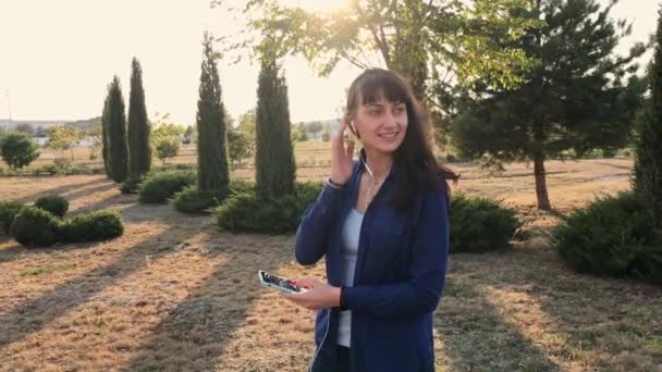 Junge glückliche brünette Frau hört Musik im Herbstpark. - Filmmaterial, Video