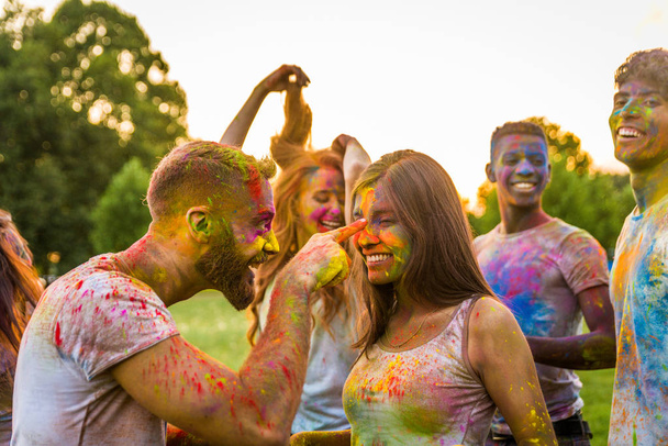 Group of happy friends playing with holi colors in a park - Young adults having fun at a holi festival, concepts about fun, fun and young generation - Foto, imagen