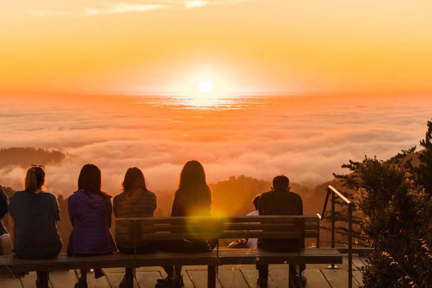 Группа людей наблюдает закат над облаками, заполняющими лесную долину
 - Фото, изображение
