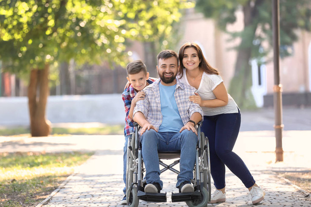 Молодой человек в инвалидной коляске со своей семьей прогуливается на свежем воздухе
 - Фото, изображение