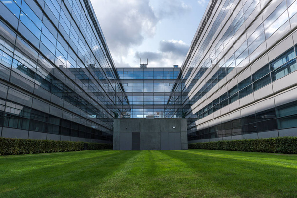 Симметрия в современной архитектуре. Отражение облаков в стеклянных окнах и зеленой лужайке впереди. Технический университет Эйндховена, Нидерланды
. - Фото, изображение