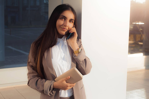 Young attractive girl in business suit uses smartphone. Lifestyle and business portrait - Zdjęcie, obraz